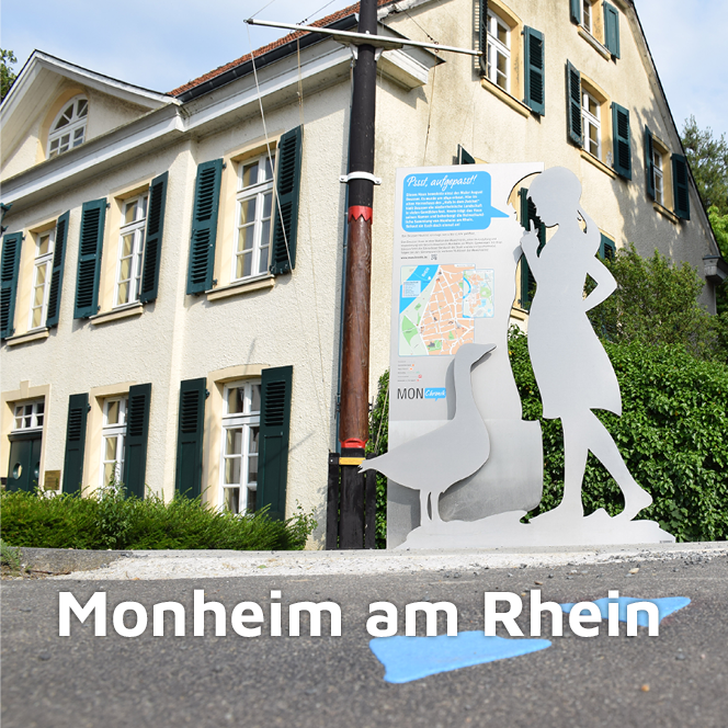 Gänseliesel mit Infotafel über die MonChronik am Deusser Haus mit blauen Gänsespuren auf dem Asphalt im Vordergrund in Monheim am Rhein
