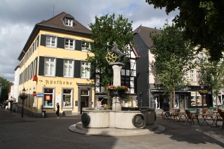 Bir çeşme ve aslan heykeli ile Ratingen pazar meydanı ve arka planda eski bir eczane