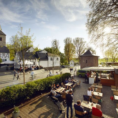 Blick von oben auf einen Biergarten in der Altstadt von Monheim am Rhein mit vielen Menschen im Sommer, im Hintergrund sind Fachwerkhäuser und ein Kirchturm zu sehen