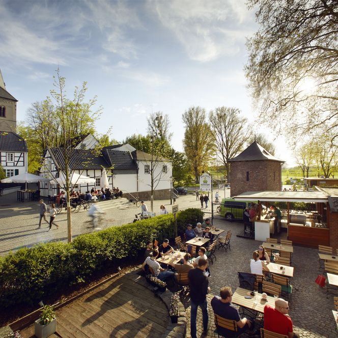 Blick von oben auf einen Biergarten in der Altstadt von Monheim am Rhein mit vielen Menschen im Sommer, im Hintergrund sind Fachwerkhäuser und ein Kirchturm zu sehen