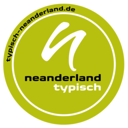 yuvarlak logo TYPISCH neanderland foku (daha küçük siyah "neanderland" yazısının üzerinde beyaz küçük n ve altında beyaz bir daire içinde beyaz "tipik" yazı ve yeşil bir arka plan üzerinde tipik-neanderland-de dışında tipik-neanderland-de)