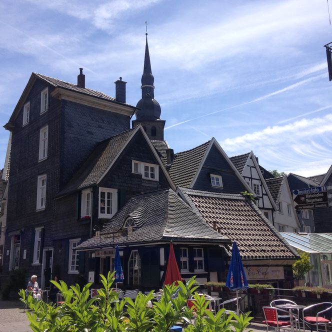 Innenstadt von Velbert-Langenberg mit Außengastronomie, Wegweiser und grüner Pflanze im Vordergrund