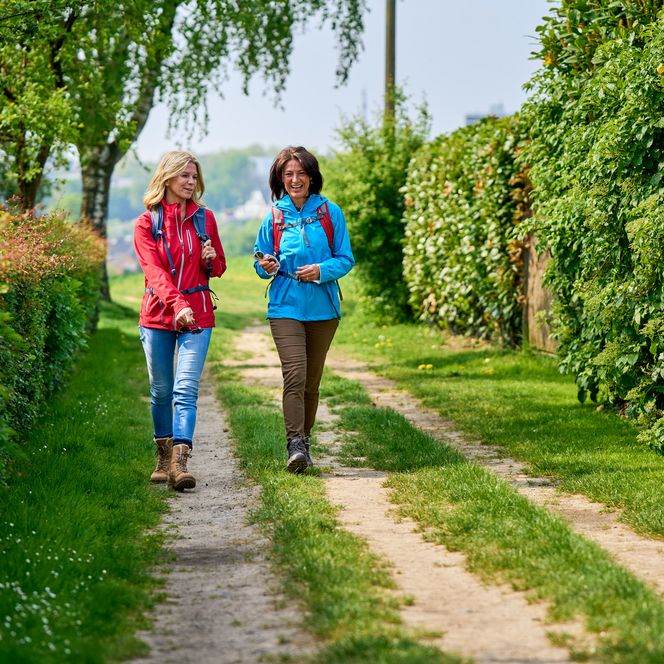 Zwei Freundinnen wandern auf einem Feldweg entlang von Hecken auf dem neanderland STEIG in Heiligenhaus