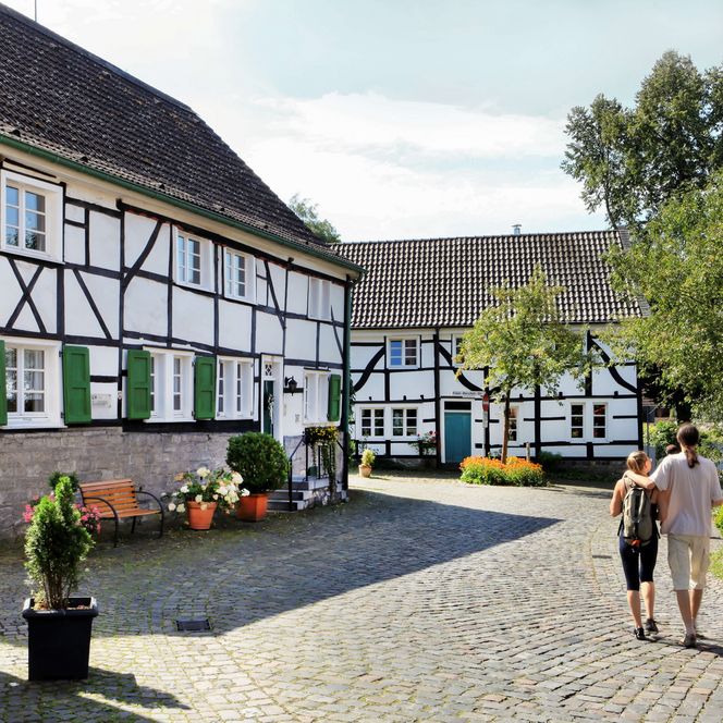 Zwei Spaziergänger von hinten vor und neben zwei Bergischen Fachwerkhäusern in Dorf Gruiten in Haan
