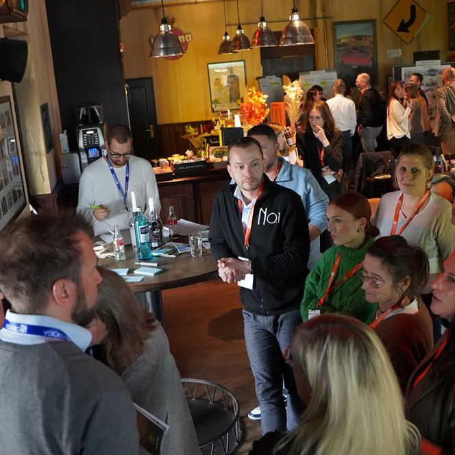 Eine Gruppe von ca. 5 Personen steht um eine Stellwand herum und diskutiert angeregt.