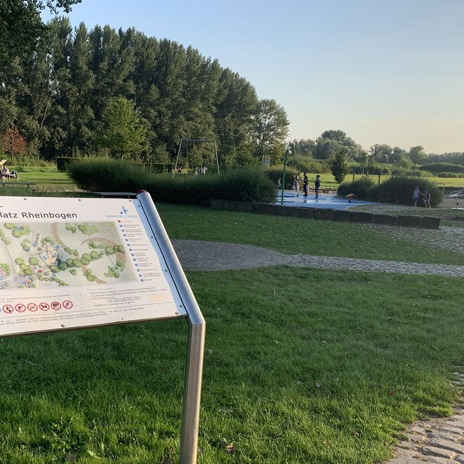 Schild des Kinderspielplatzes Rheinbogen mit Klettergerüst im Hintergrund in Monheim am Rhein