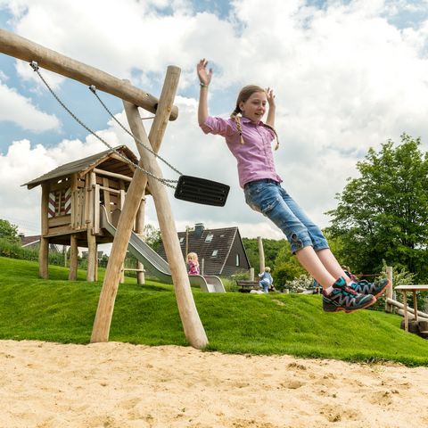 Girl jumps from a swing on a playground in neanderland