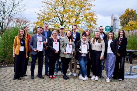 Photo de groupe de 14 personnes regardant l'objectif avec un air amical ; en arrière-plan, un grand arbre aux feuilles jaunes aux couleurs de l'automne.