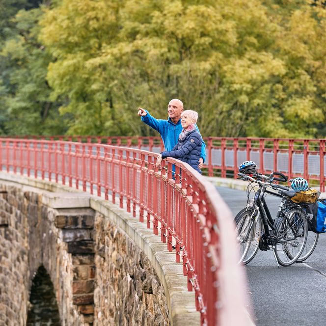 Zwei Fahrradfahrer stehen am Geländer des Viadukt Ruhrstraße Süd auf dem PanoramaRadweg niederbergbahn und genießen den Fernblick