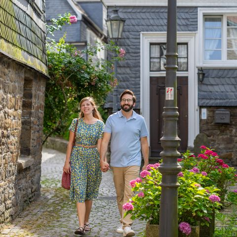 Couple walking hand in hand through an alley in Velbert-Langenberg past a lantern with a waymarking of the neanderland STEIG discovery loop.