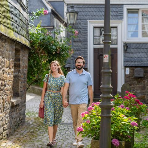 Paar läuft Hand in Hand durch eine Gasse in Velbert-Langenberg vorbei an einer Laterne mit Wegmarkierung der neanderland STEIG Entdeckerschleife.