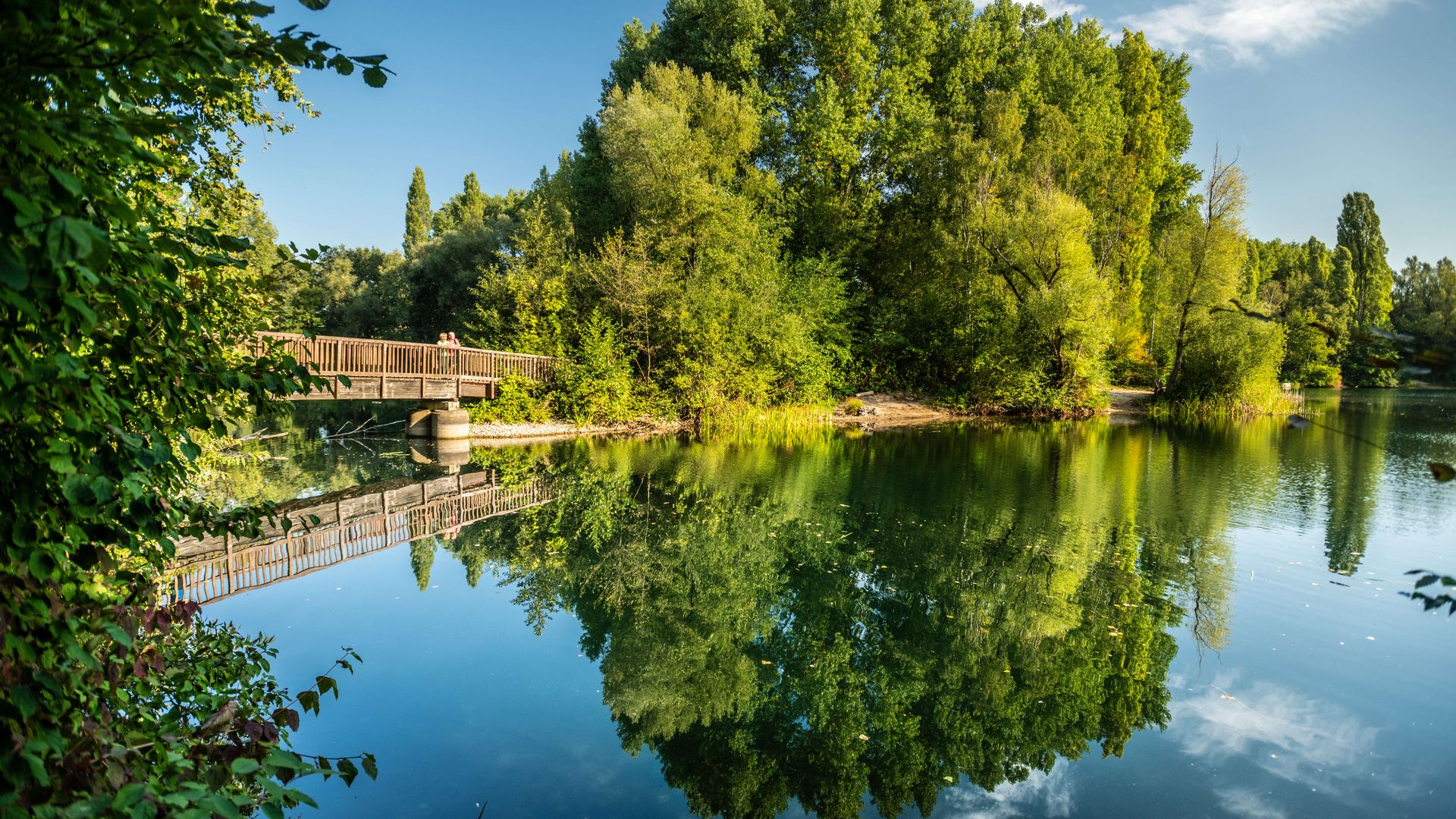 Menzelsee und Holzbrücke mit Personen und Bäumen im Hintergrund in Hilden