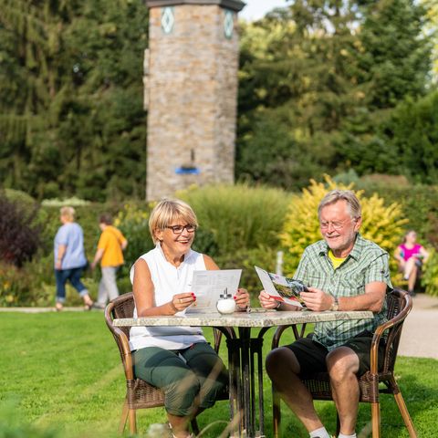 Een man en vrouw zitten buiten aan een tafel in het binnenplaatscafé Abtsküche in Heiligenhaus met de toren op de achtergrond