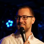 Portrait des Poetry Slammers Jan Schmidt mit Mikrofon vor dunklem Hintergrund
