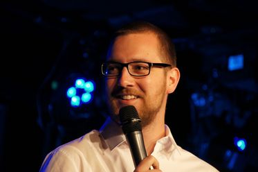 Portrait des Poetry Slammers Jan Schmidt mit Mikrofon vor dunklem Hintergrund