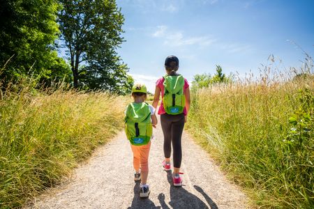 Dos niños caminan por un camino de campo y llevan mochilas verdes, las mochilas de descubrimiento de la ciudad de Monheim am Rhein