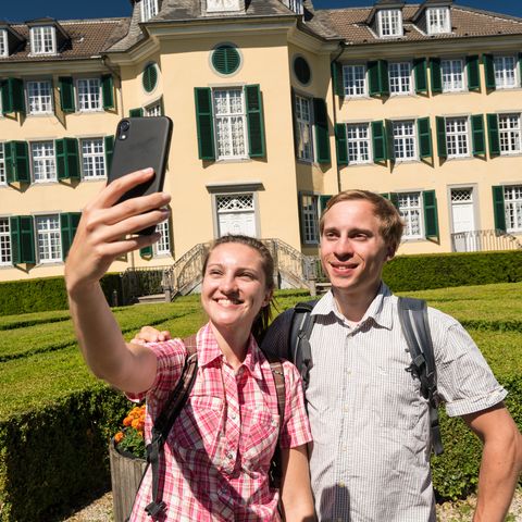 Young couple photograph themselves with the historic building of the Cromford textile factory in Ratingen in the background