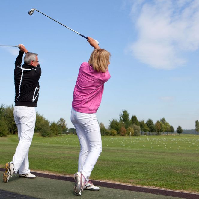 Zwei Erwachsene heben auf einem Golfplatz simultan die Golfschläger in die Luft