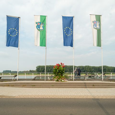 Sechs Flaggen positioniert am NRW-Rheinradweg präsentieren Deutschland, die EU und die Stadt Monheim am Rhein