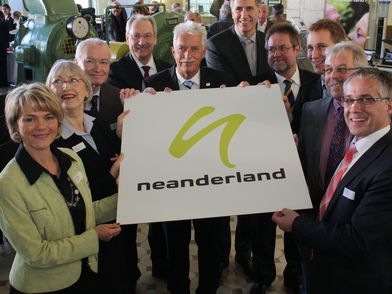 Los fundadores de la marca "Neanderland" junto con el administrador del distrito sostienen el cartel de Neanderland.