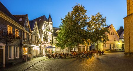 Place illuminée de la ville haute de Mettmann Abens avec gastronomie dans de vieilles maisons en ardoise et à colombages et deux arbres devant
