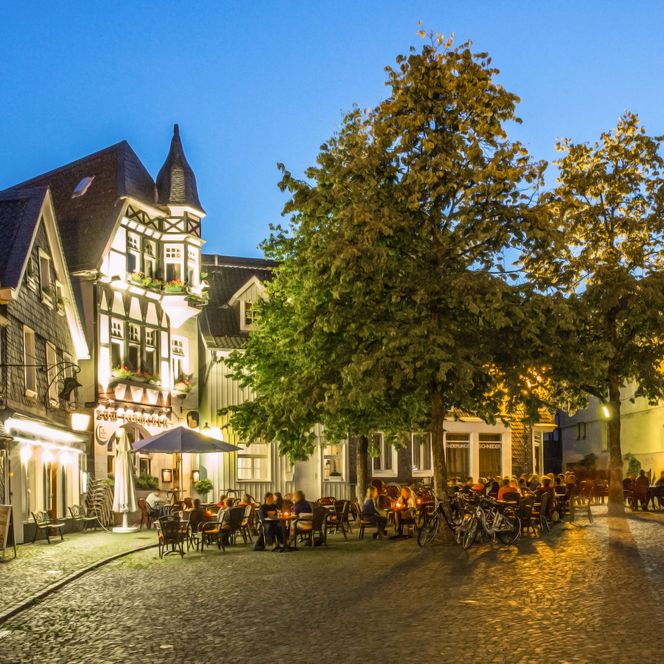 beleuchteter Platz in der Oberstadt von Mettmann Abens mit Gastronomie in alten Schiefer- und Fachwerkhäusern und zwei Bäumen davor