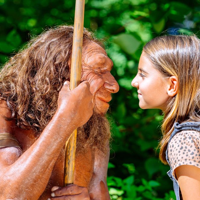Mädchen betrachtet Gesicht der Neandertaler-Figur draußen vor Bäumen am Neanderthal Museum in Mettmann