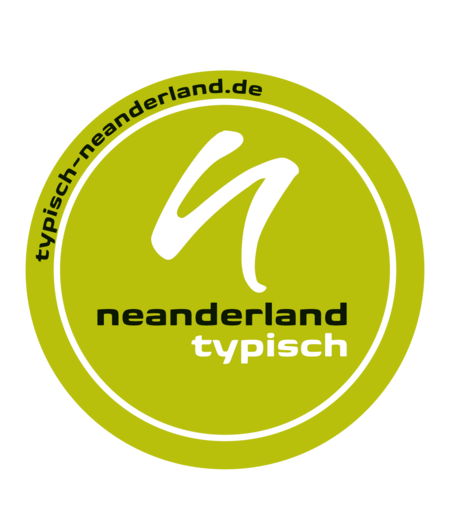 rundes Logo TYPISCH neanderland-Siegel (weißes kleines n über kleineren schwarzen "neanderland"-Schriftzug mit weißen "typisch"-Schriftzug darunter in einem weißen Kreis mit typisch-neanderland-de außen auf grünem Hintergrund)